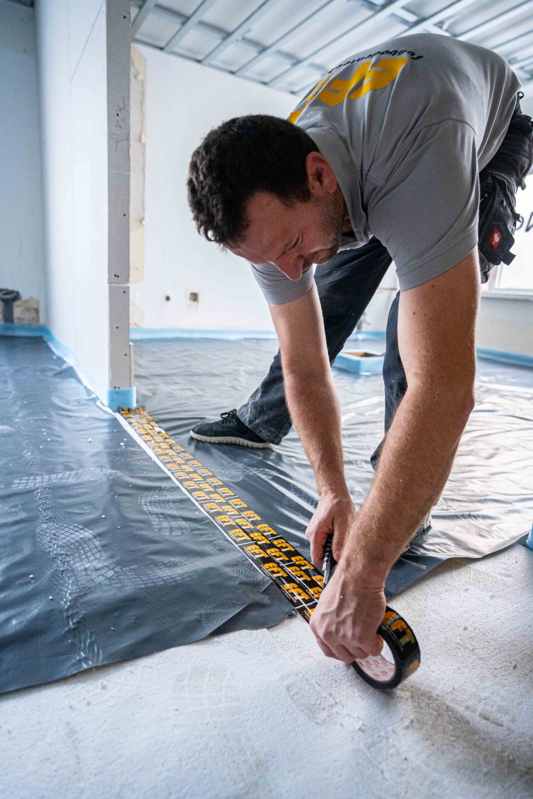 Mitarbeiter verklebt Randstreifen und Dampfsperre vor dem Estricheinbau